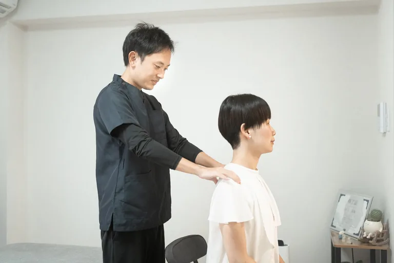 施術者が座った姿勢で肩まわりの状態を確認している様子